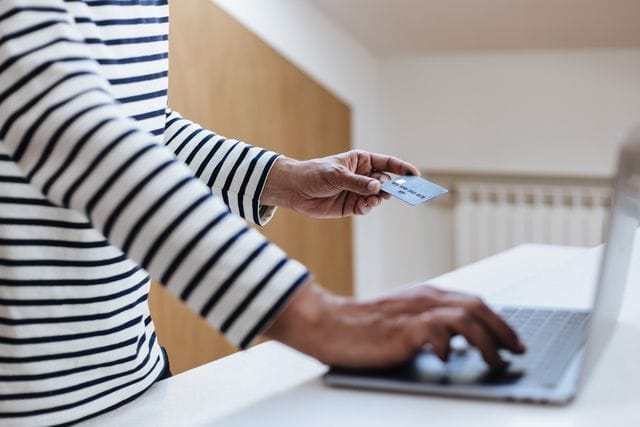 Person using a credit card for online shopping on a laptop indoors.